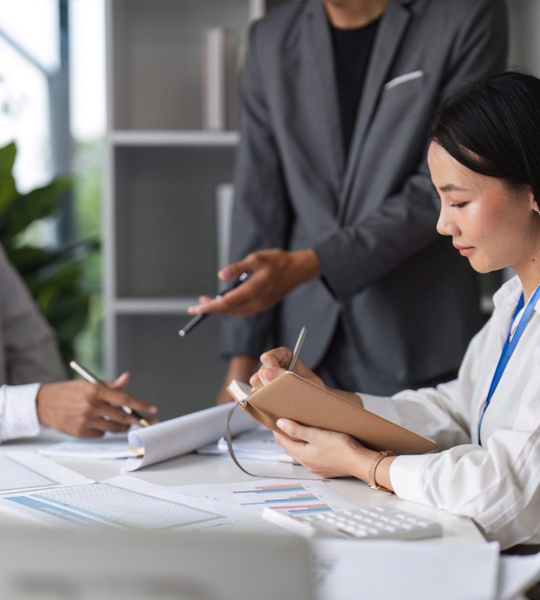 Professional business people collaborating in a modern office setting, engaged in a meeting and taking notes.