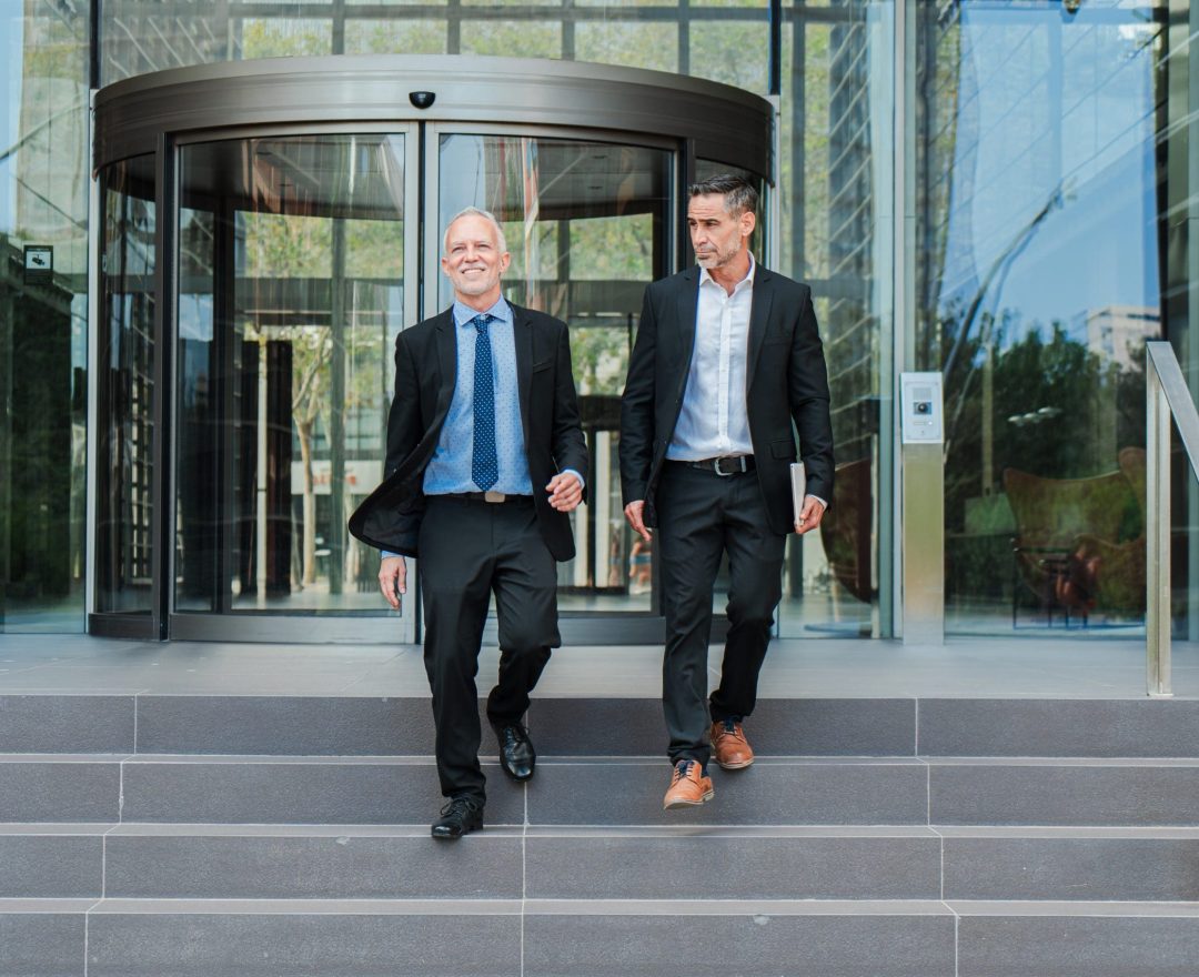 Confident and successful business men walking down the staircase, talking about the corporate finance. Office colleagues on a stairway having a conversation. Middle aged executive males discurssing Company Registration Hong Kong