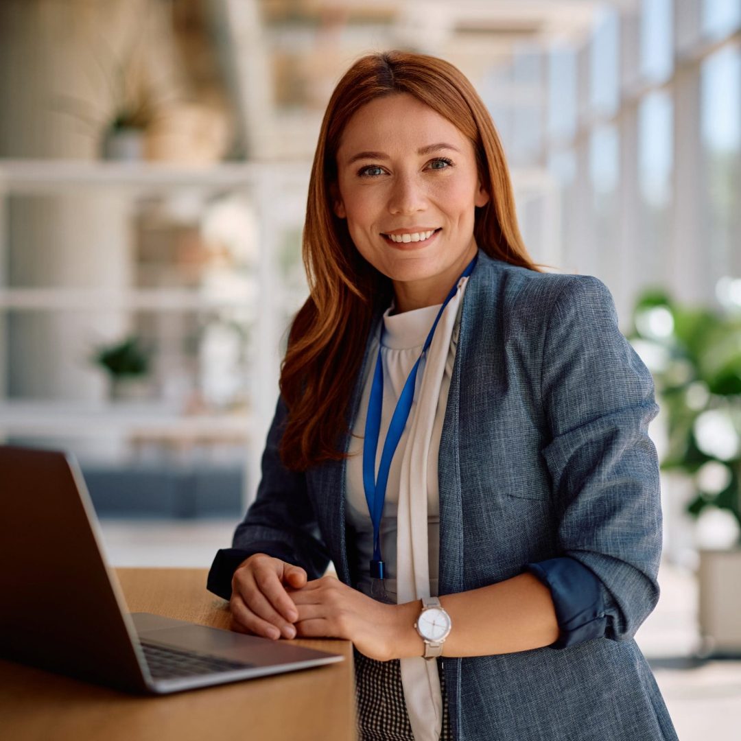 Happy female entrepreneur using laptop while working in the office and looking at camera.