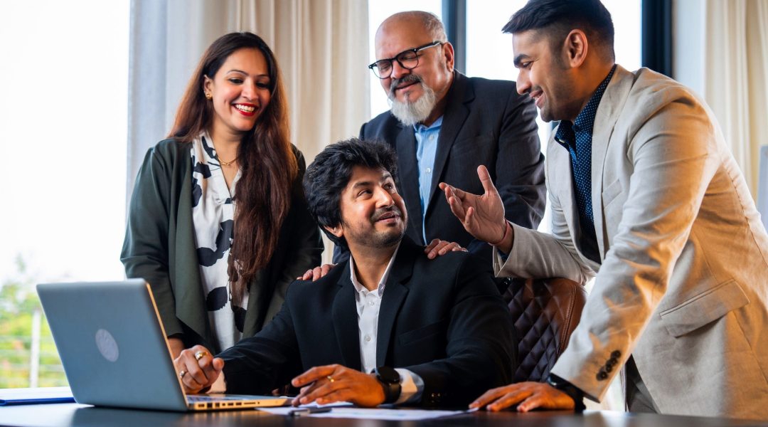 Indian Asian group of successful corporate professionals in formal attire working on laptop, reviewing business documents or reports, and discussing serious matters in an office setting