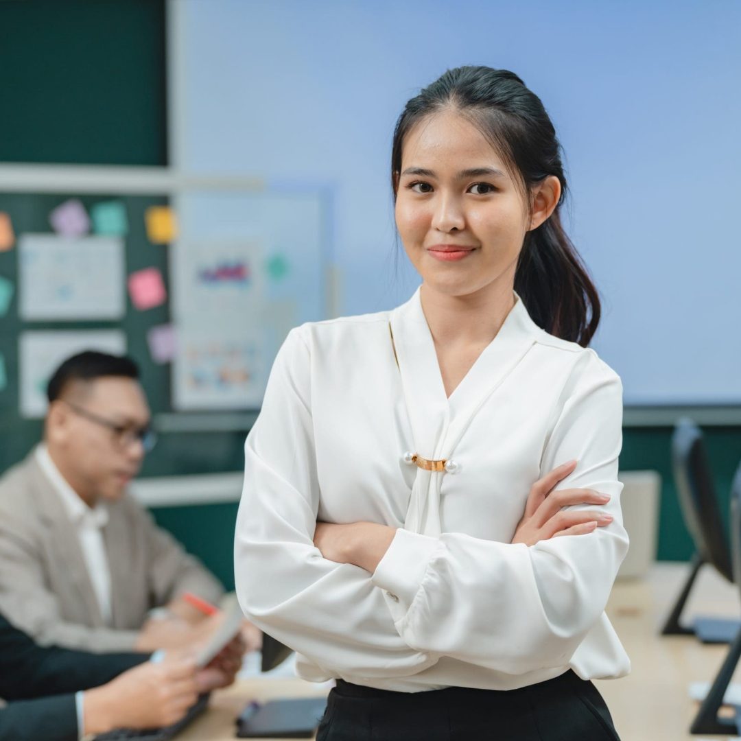 Happy confident smiling young professional Asian business woman corporate leader, Japanese female employee or company sales marketing manager standing arms crossed in office, cute girl portrait