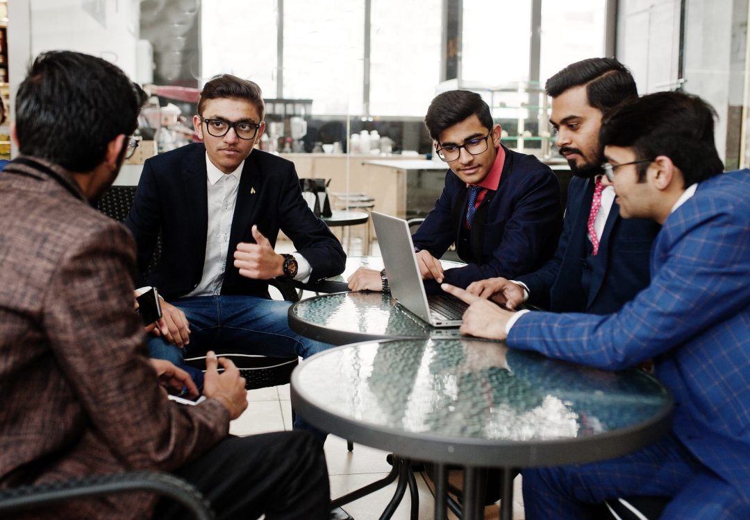 Group of five indian business man in suits sitting at office on cafe and looking at laptop.