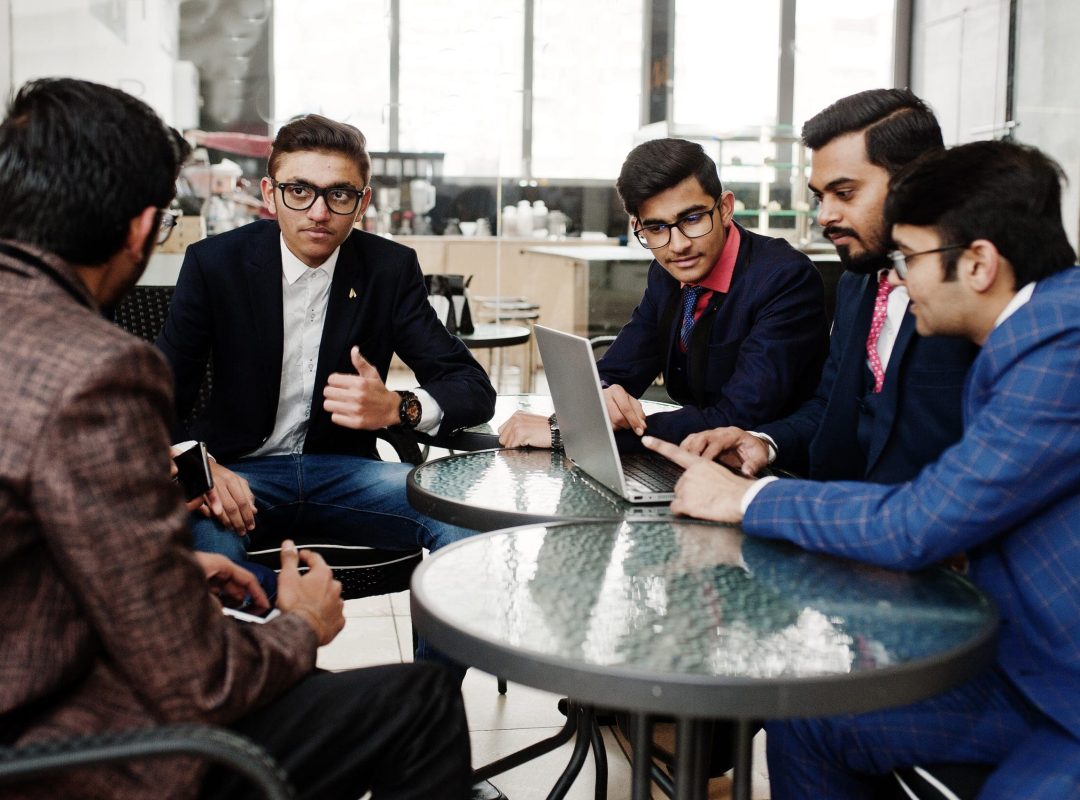 Group of five indian business man in suits sitting at office on cafe and looking at laptop.