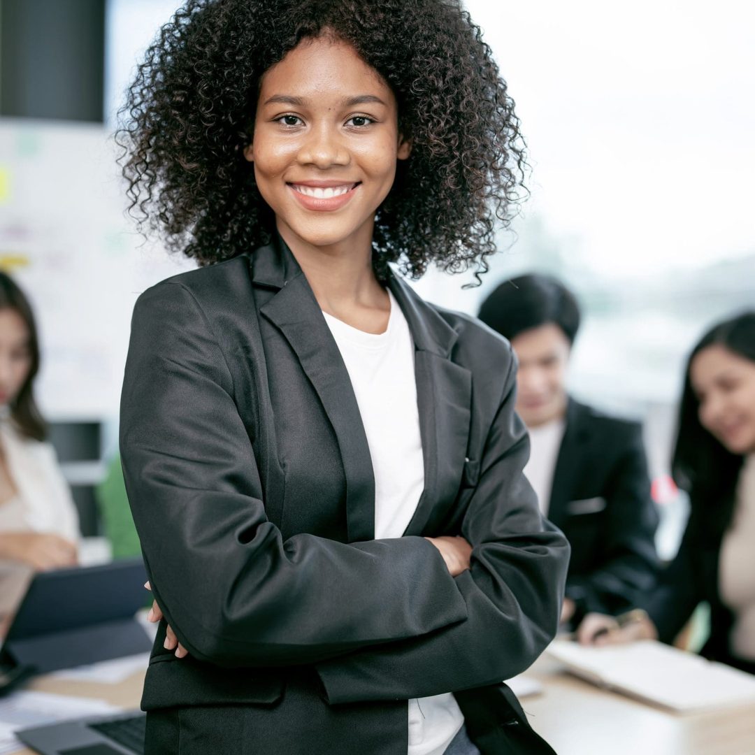 Successful businesswoman standing in creative office and smiling to camera. Portrait of beautiful african woman standing in front of business team at office.