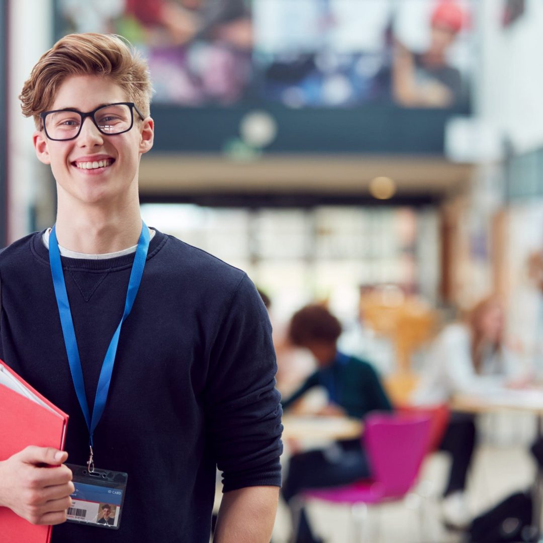 Portrait Of Smiling Male College Student In Busy Communal Campus Building