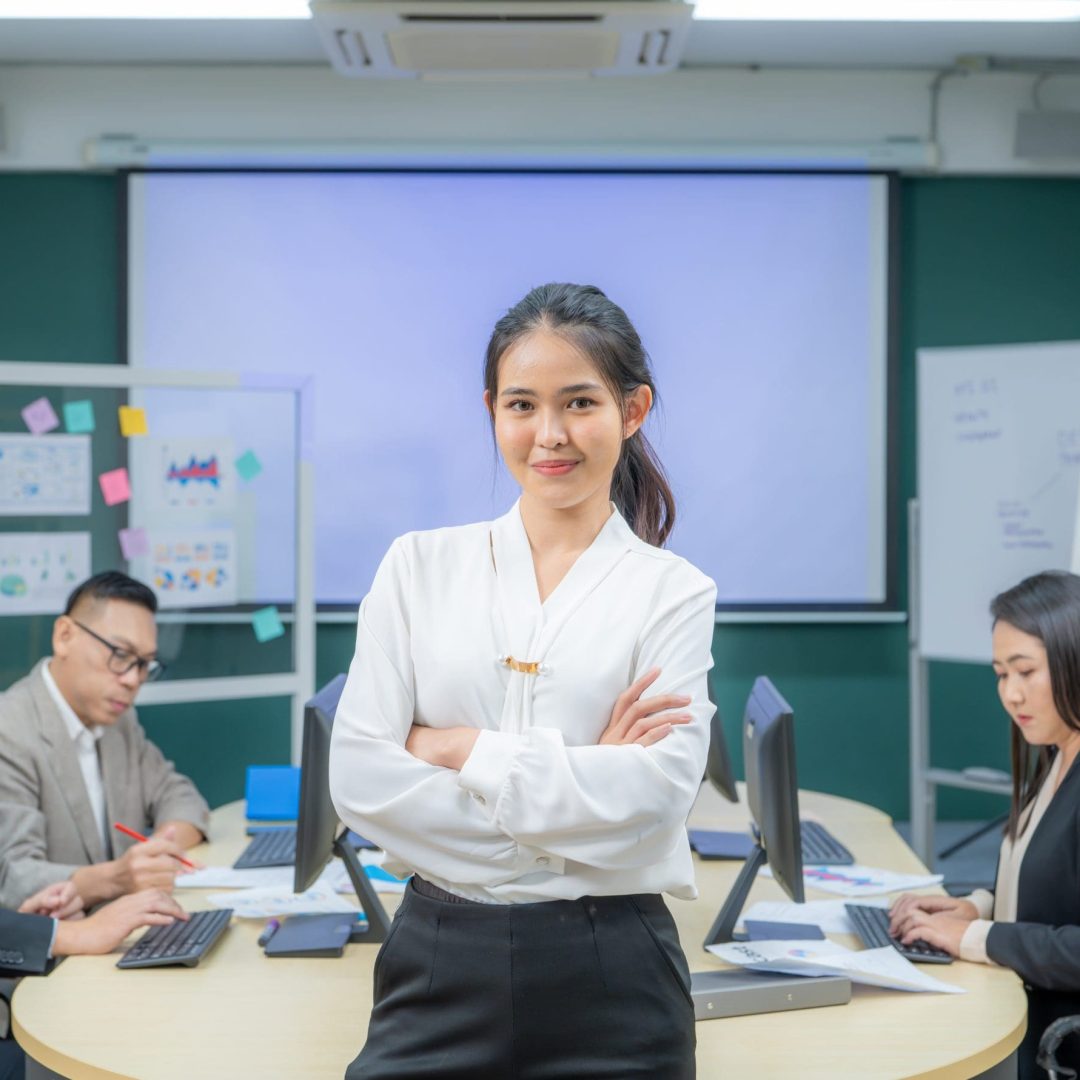 Portrait smiling modern business woman standing in an office at team meeting. Confident young Asian businesswoman with colleagues in boardroom. Meeting in conference room. Office conference room.