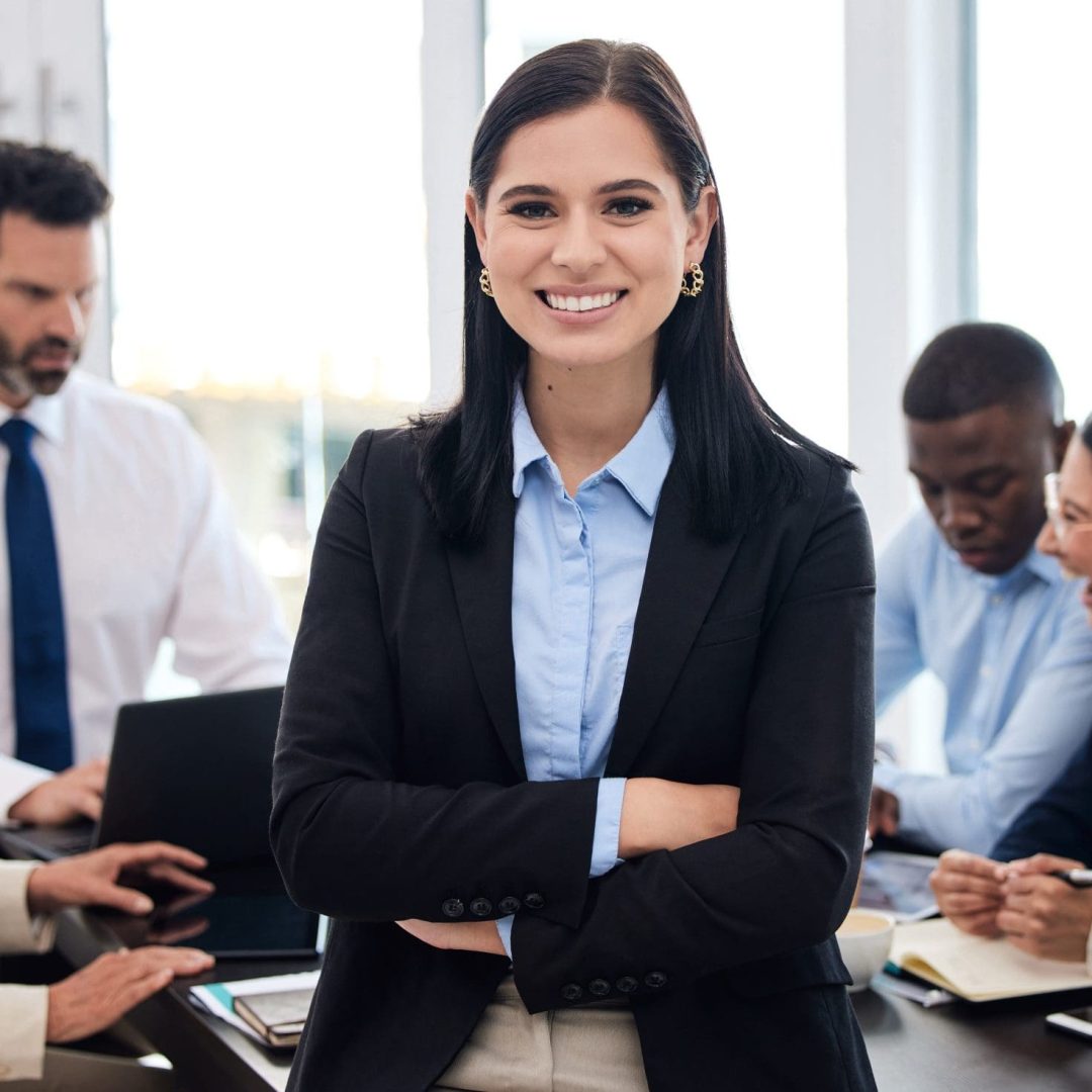 Shot of a young businesswoman standing with her arms crossed in a meeting at work.
